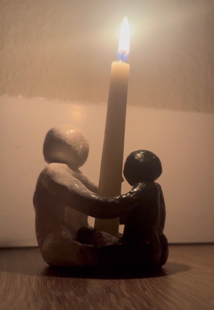 Clay people with limbs attached to each other in a circle, holding a lit candle